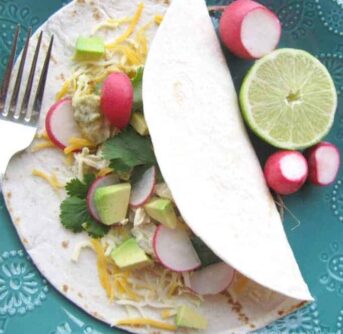 A tortilla lying on a table with radishes and lemon beside it.