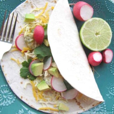 A tortilla lying on a table with radishes and lemon beside it.