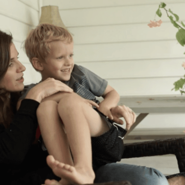 A woman sitting on a porch chair holding a little boy on her lap.