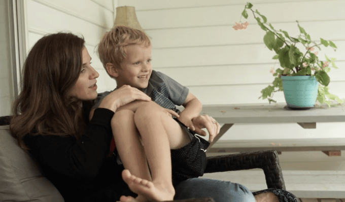 A woman sitting on a porch chair holding a little boy on her lap.