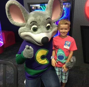 A little boy standing beside Chuck E Cheese posing for the camera.