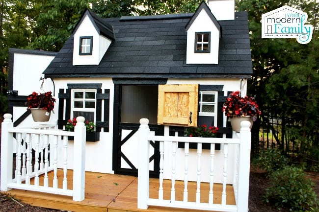 A white and black playhouse with a front porch and windows.