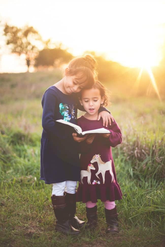 Two girls standing in a field looking at a book.
