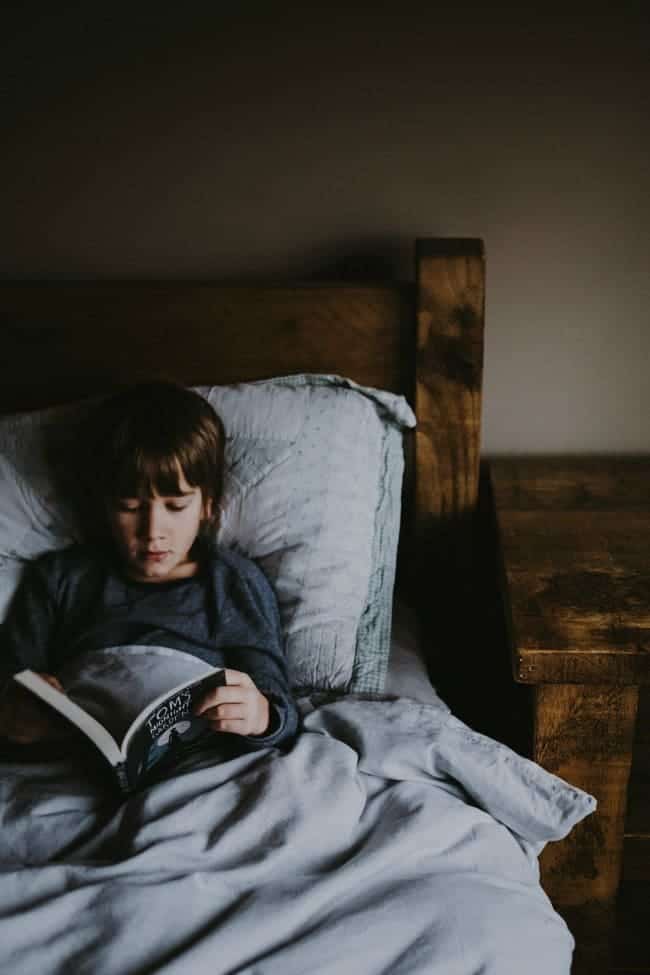 A young boy lying on a bed reading a book.