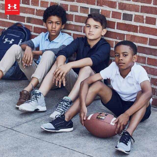 A group of boys sitting next to a brick wall with a football in front of them.