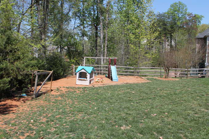 A swing set with a slide and a plastic playhouse in a back yard.