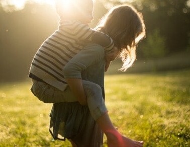 A woman carrying a child on her back in a grassy field.