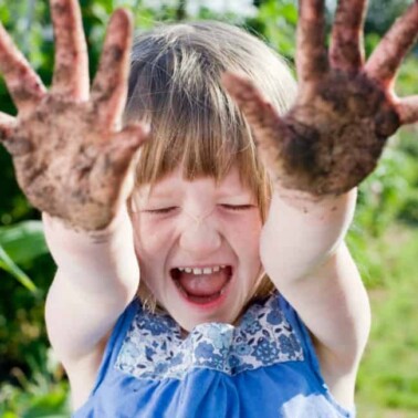 A little girl laughing with muddy hands.