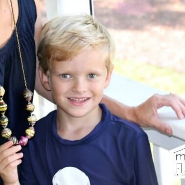 A child showing a necklace that is around a woman's neck.