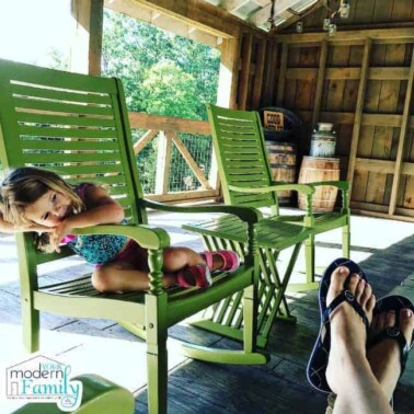 A little girl sitting on a green outdoor chair.