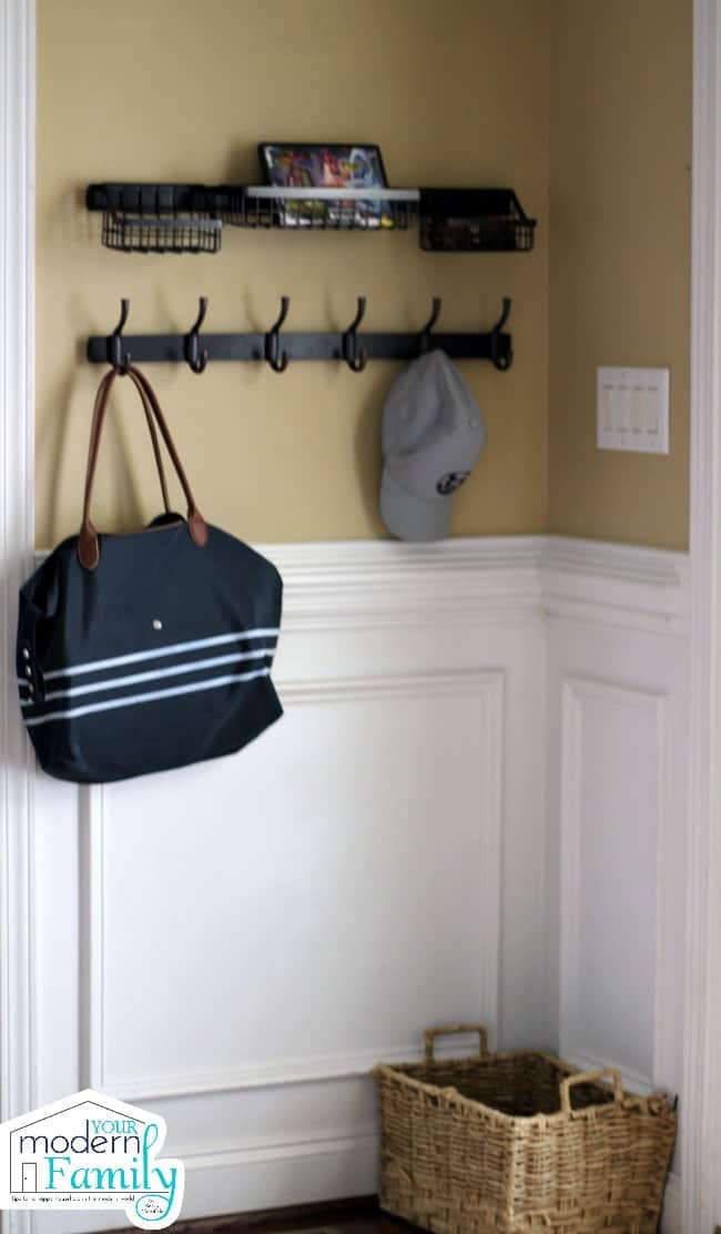 A purse and a ball cap hanging on a wooden rack with hooks on the wall.