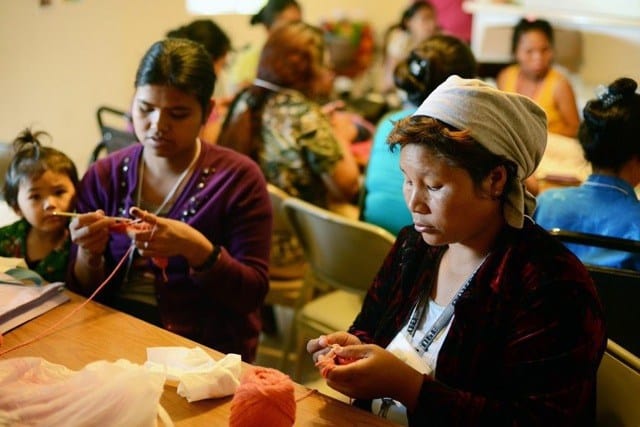 A group of people sitting at a table sewing items.