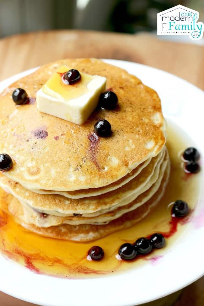 A stack of blueberry pancakes with syrup and butter on a white plate.