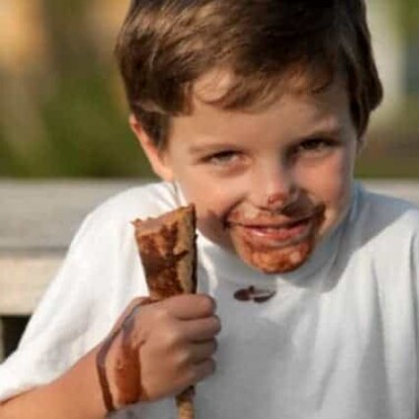 A boy eating an ice cream cone with it melting on his face, hand and shirt.