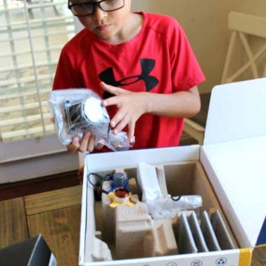 A young boy standing by a box filled with kid's building supplies.