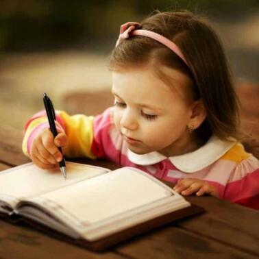 A little girl sitting at a table writing in a book.
