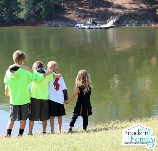 A group of kids standing close to each other next to a lake.