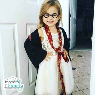 A little girl dressed up like Harry Potter standing in front of a white door.