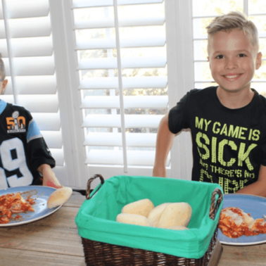 Two young boys sitting at a table with plates of food.