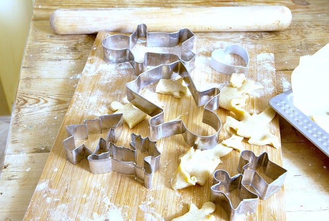 A variety of Christmas themed cookie cutters on a wooden cutting board.