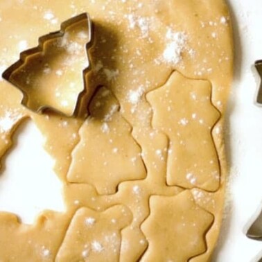 Rolled out cookie dough with a Christmas tree cookie cutter resting on it.