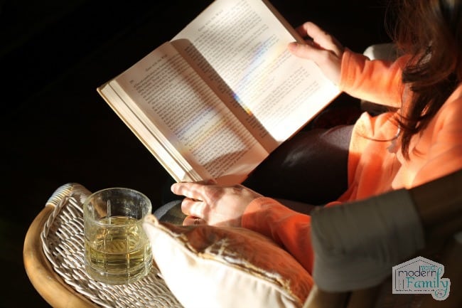 A woman reading a book with a glass of wine beside her.