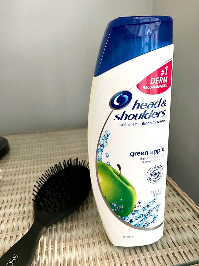A close up of a bottle of Head and Shoulders with a brush beside it.