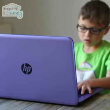 A young boy sitting at a table using a laptop computer.