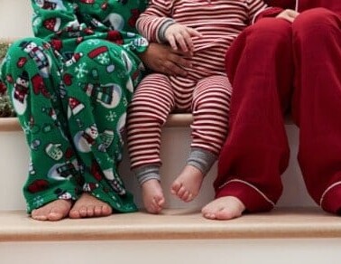 Three kids in Christmas pajamas sitting on wooden stairs.