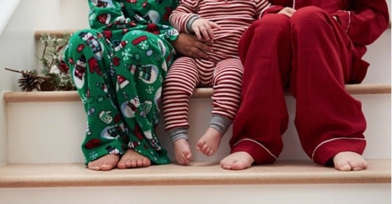 Three kids in Christmas pajamas sitting on wooden stairs.