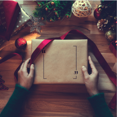 Hands wrapping a present with Christmas decorations around it.