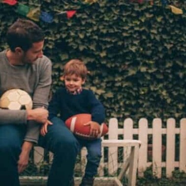 A man sitting on a bench with a little boy holding a football.