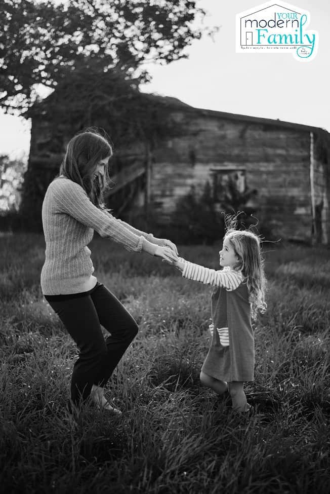 A lady and a little girl holding hands in front of a barn.