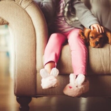 A dog lying on a couch beside a little girl.