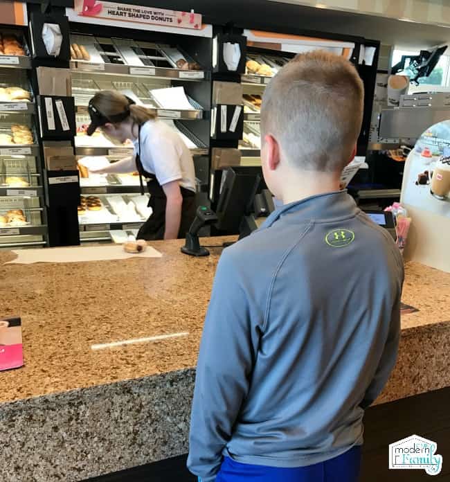 A boy standing in front of a donut shop counter.