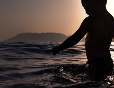 A child walking in a body of water at sunset.