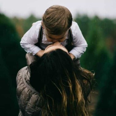 A woman lifting a child up to kiss him.