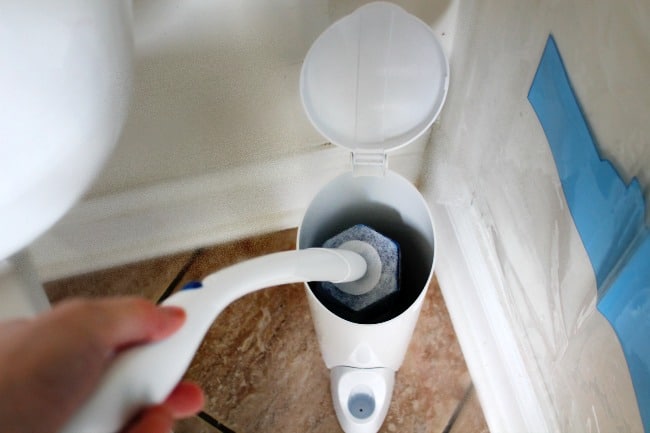 A person placing a toilet brush into its holder.