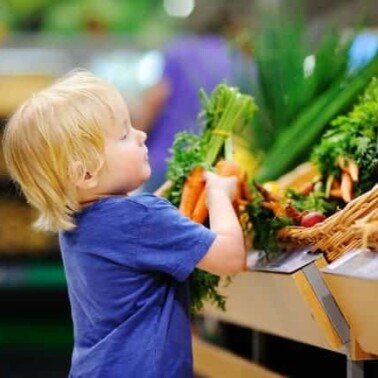 A little boy getting carrots from a vegetable stand in a grocery store.