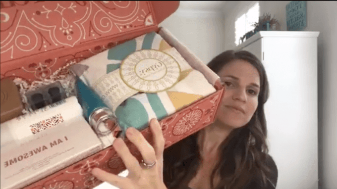 A woman taking a selfie holding a FabFitFun Box with items in it.