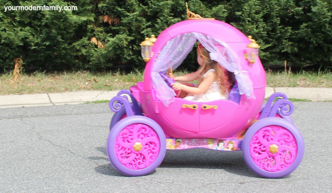 A little girl riding in a pink carriage child\'s ride on toy.