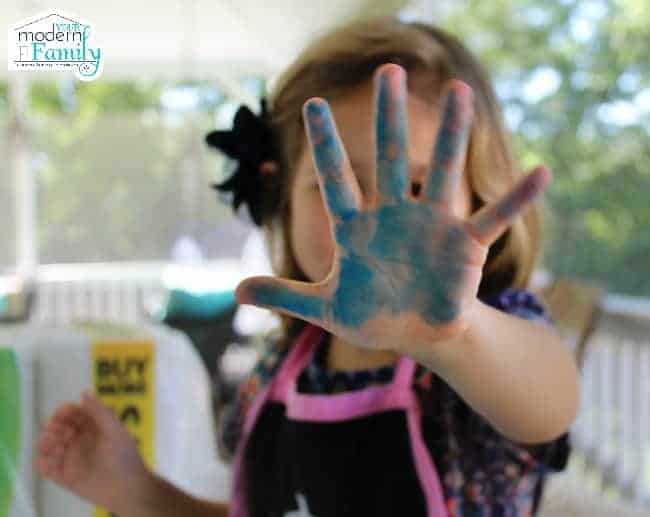 A little girl showing that her hand is painted blue.