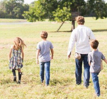 A group of people walking away from the camera in a grass covered field.