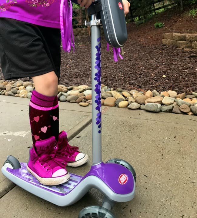 A little girl that is standing on a Radio Flyer scooter.