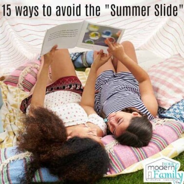 Two girls lying on a blanket in the grass reading a book.