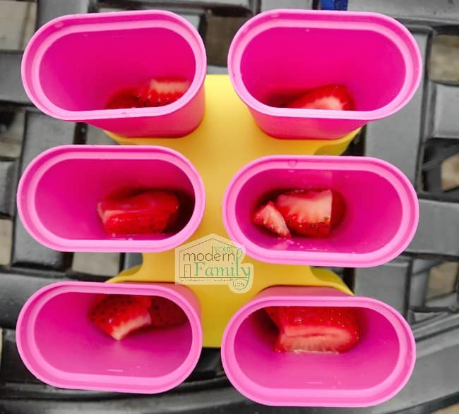 Top view of open freezer pop molds with strawberries in them.