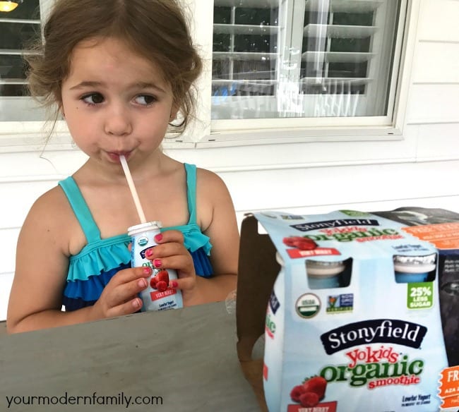 A little girl sitting at a table drinking a Stonyfield smoothie.