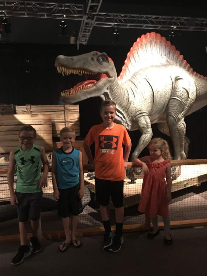 Children standing in front of a dinosaur statue.
