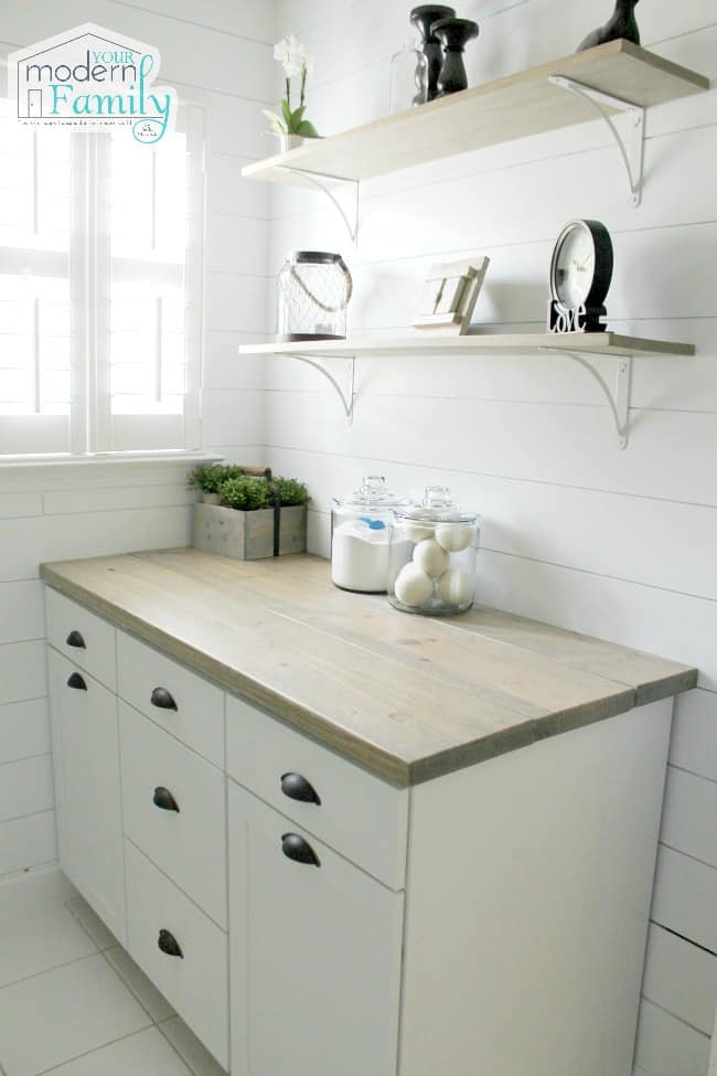 A laundry counter and shelving above it with small items on them.