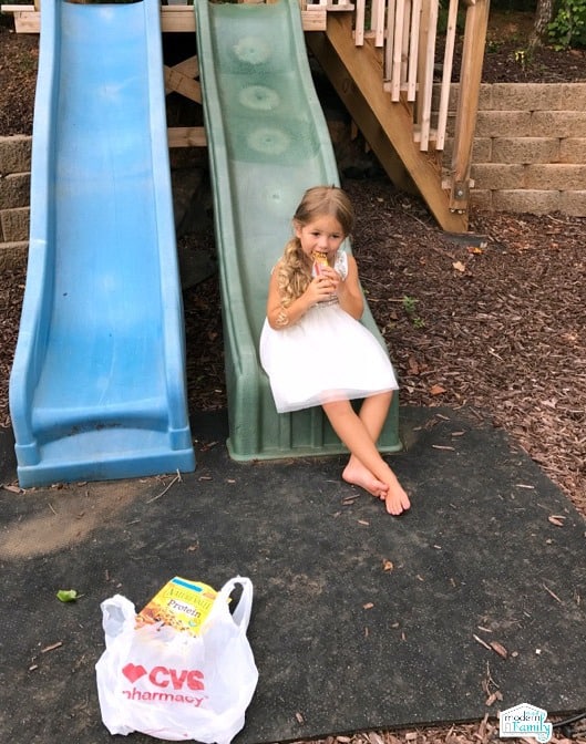 A little girl sitting at the bottom of a slide eating a snack.
